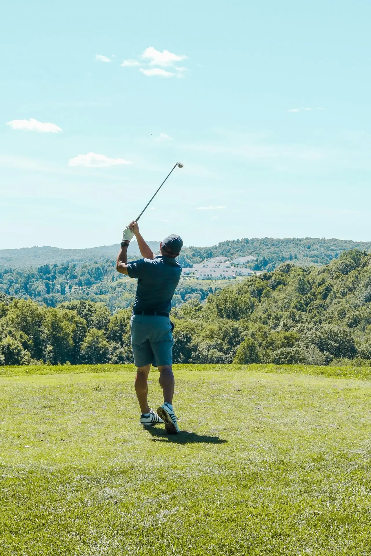 man in black shirt and brown shorts holding golf club on green grass field during daytime